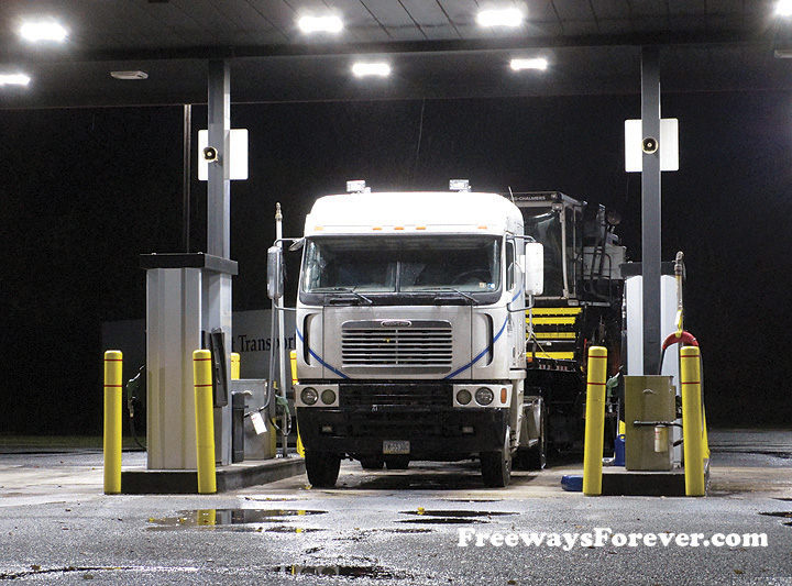 Mid-Atlantic Tech Services Freightliner with Allis-Chalmers Gleaner combine on flatbed trailer at diesel fueling station truck stop